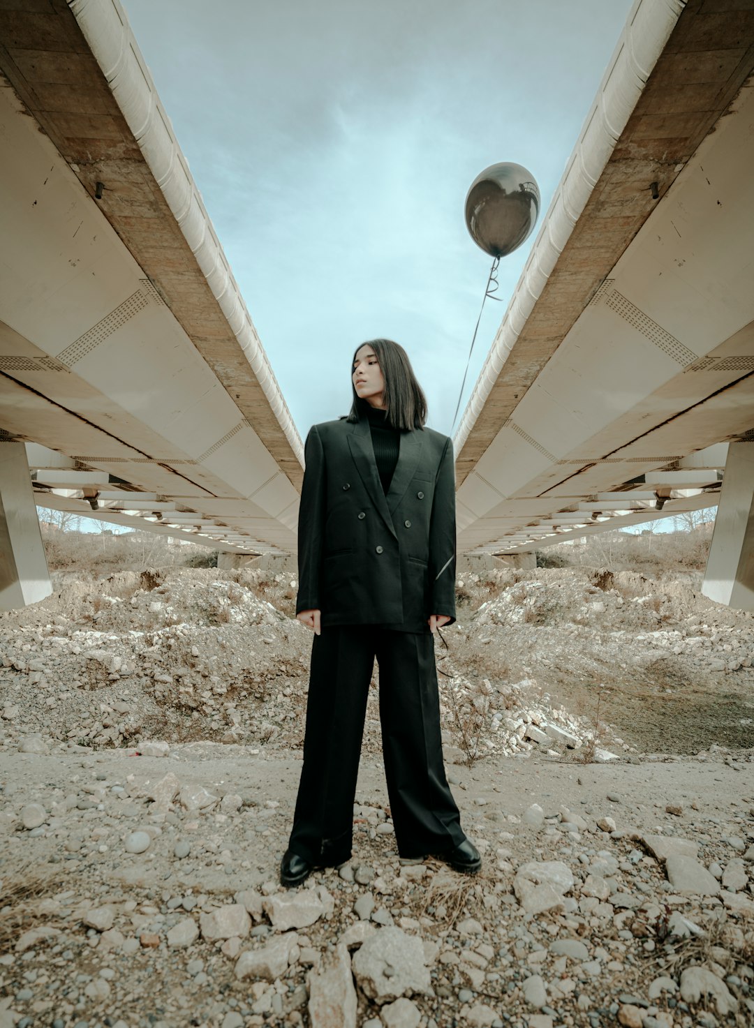 woman in black coat standing under white concrete bridge during daytime