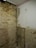 A partially unfinished room with exposed brick walls and a section of plaster that has been chipped away. The ceiling has white tiles, and some construction debris is visible on the floor.