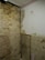 A partially unfinished room with exposed brick walls and a section of plaster that has been chipped away. The ceiling has white tiles, and some construction debris is visible on the floor.