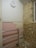 A partially renovated room with a tiled pink wall featuring some missing tiles, a metal railing, exposed brick on one wall, and a basic round wall clock showing the time as approximately 10:10. Debris is scattered on the floor, indicating ongoing construction or renovation work.