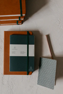 A colorful stack of premium notebooks with vibrant covers and textured pages on a wooden desk.