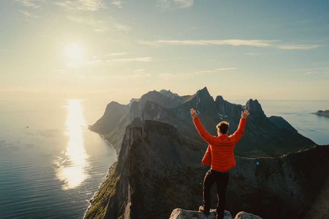 man in orange hoodie standing on rock formation during daytime