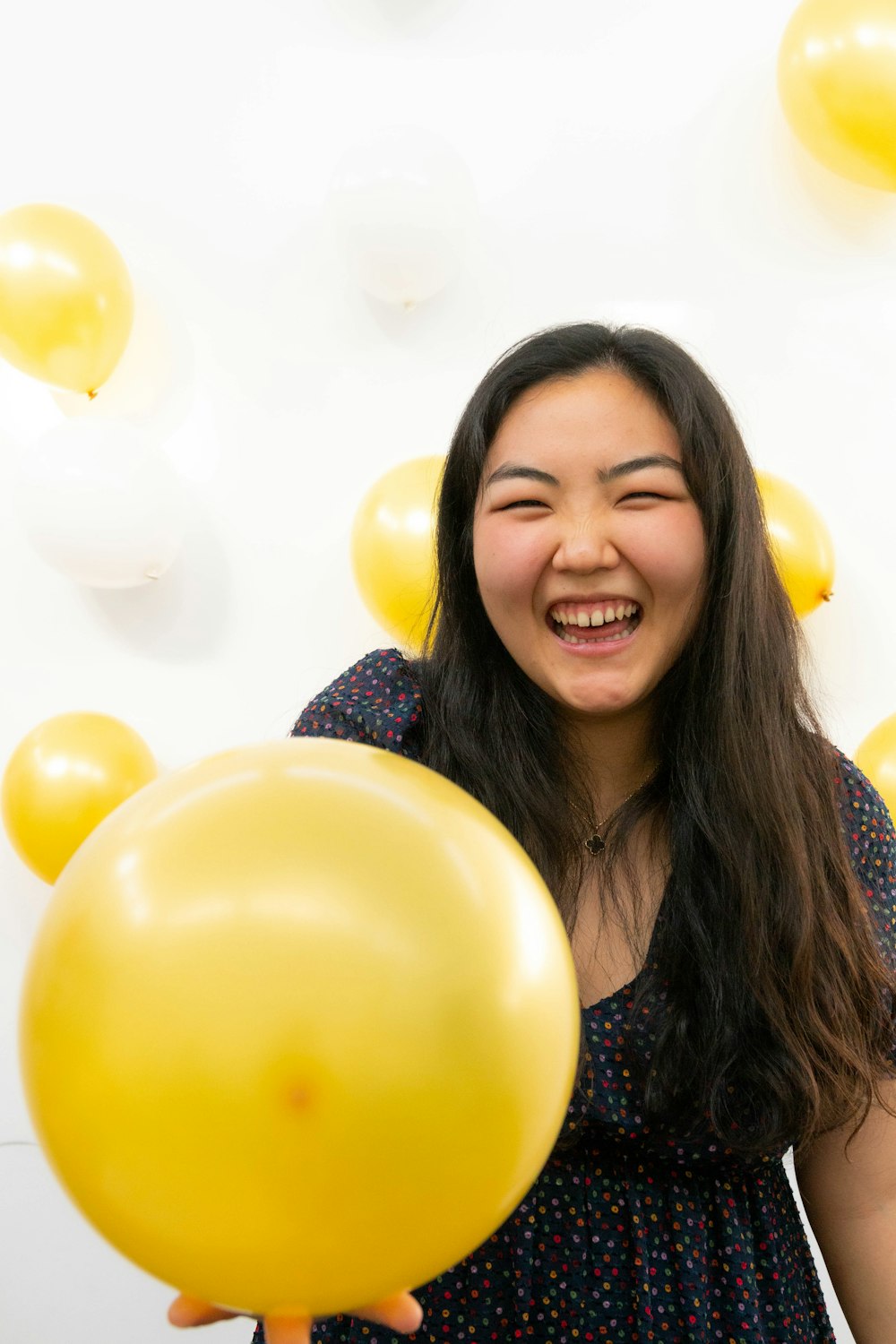 smiling woman in blue and white floral shirt holding balloons