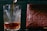 A glass with intricate cut designs is being filled with a dark liquid, possibly a beverage. Next to it is a brown, intricately carved object with floral patterns and text.