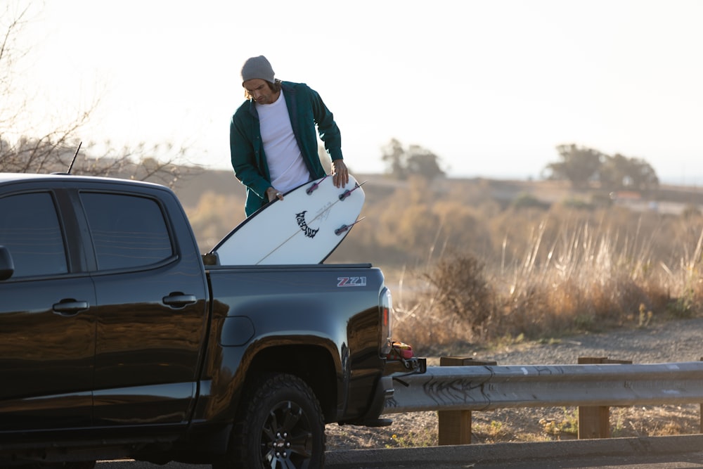 man in blue jacket and black pants sitting on white single cab pickup truck during daytime