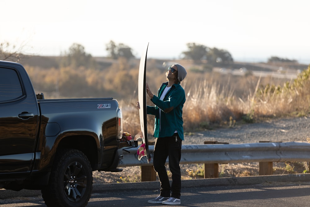 man in blue jacket and black pants holding white and black stick standing on gray pickup