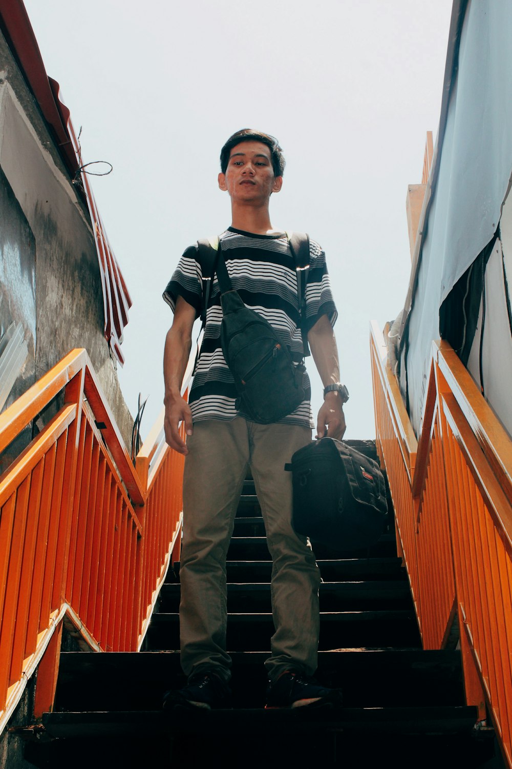 man in black and white striped polo shirt and brown pants standing on brown wooden stairs