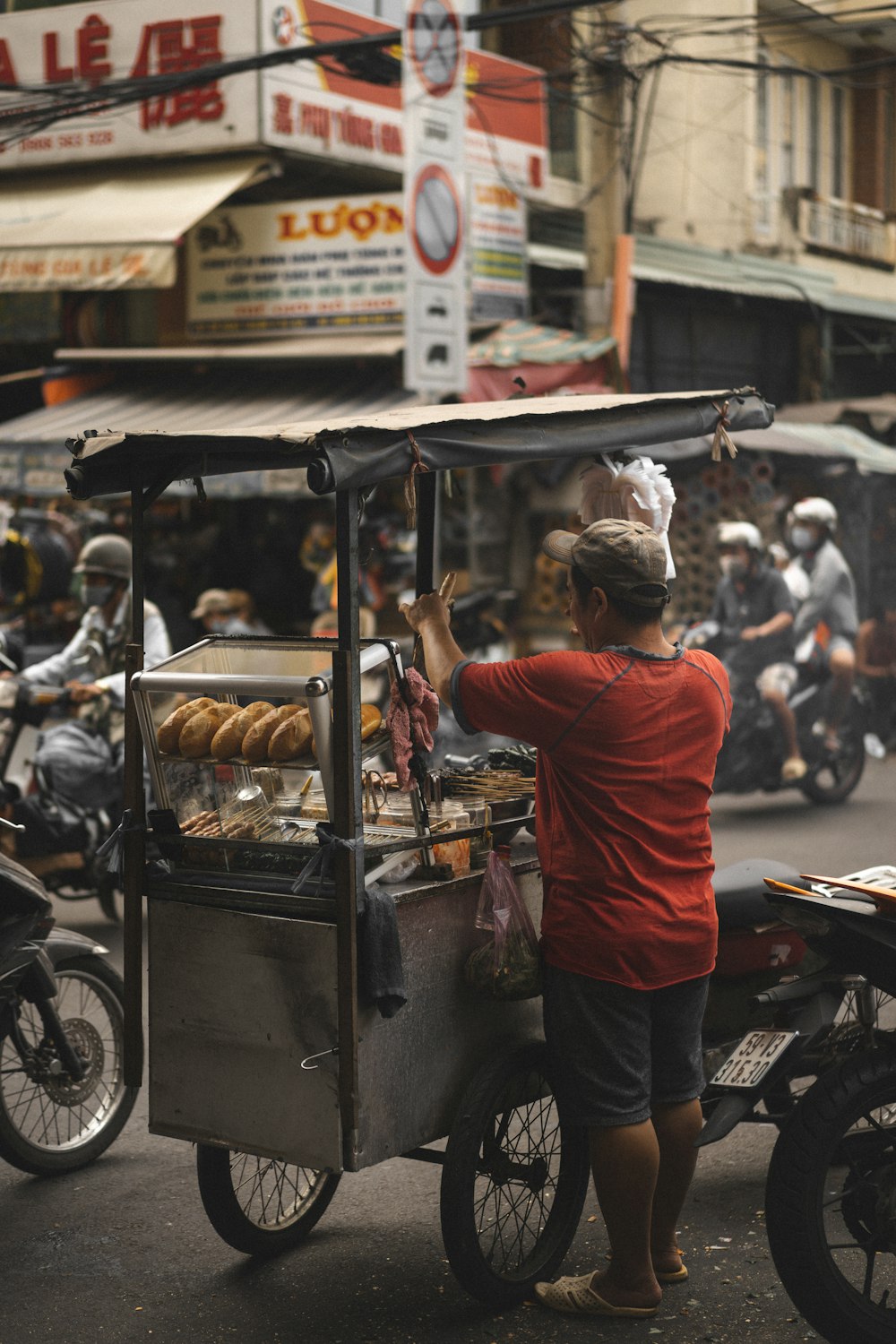 man in red t-shirt and black pants standing in front of food stall during daytime