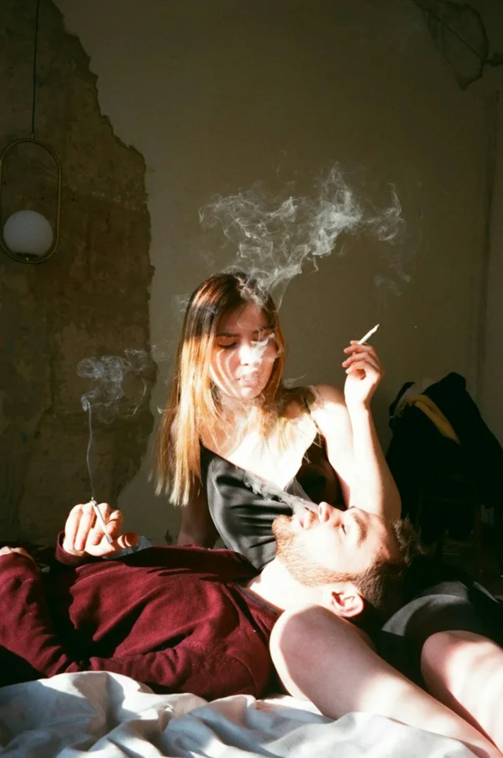 a man and a woman smoking cigarettes on a bed