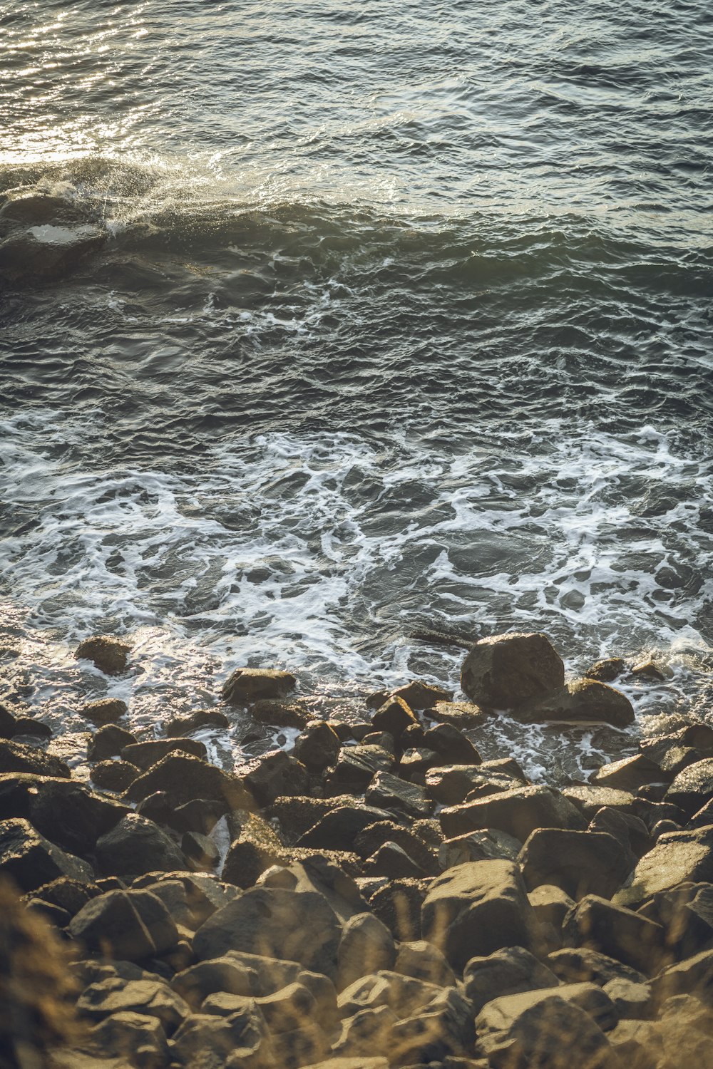 brown rocky shore with ocean waves crashing on rocks during daytime