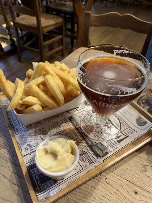 A cold craft beer with frothy head served in a branded glass next to a bowl of crispy fries