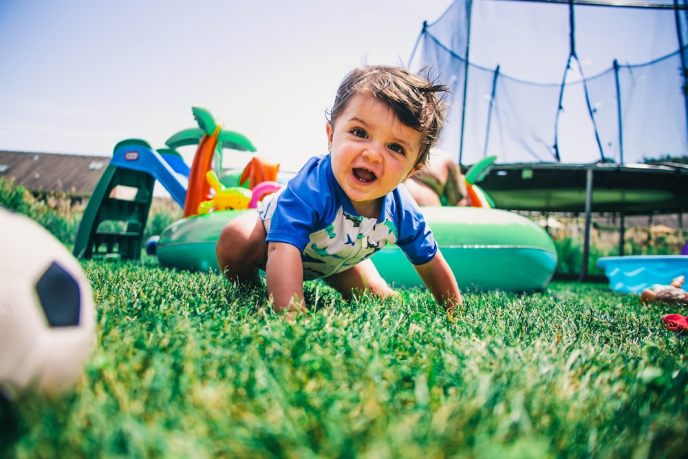 boy in blue and white crew neck t-shirt sitting on green grass field during daytime