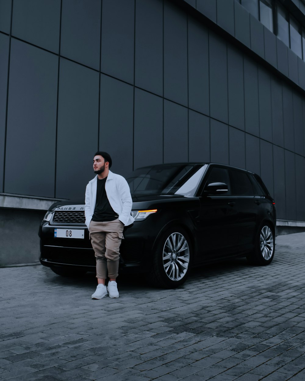 man in white dress shirt and black pants standing beside black car