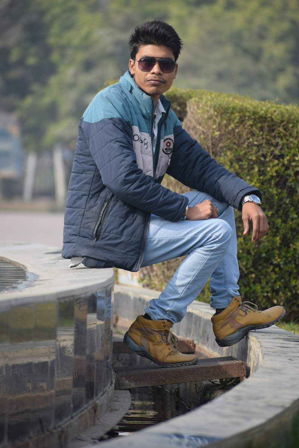 man in black jacket and blue denim jeans sitting on concrete bench during daytime