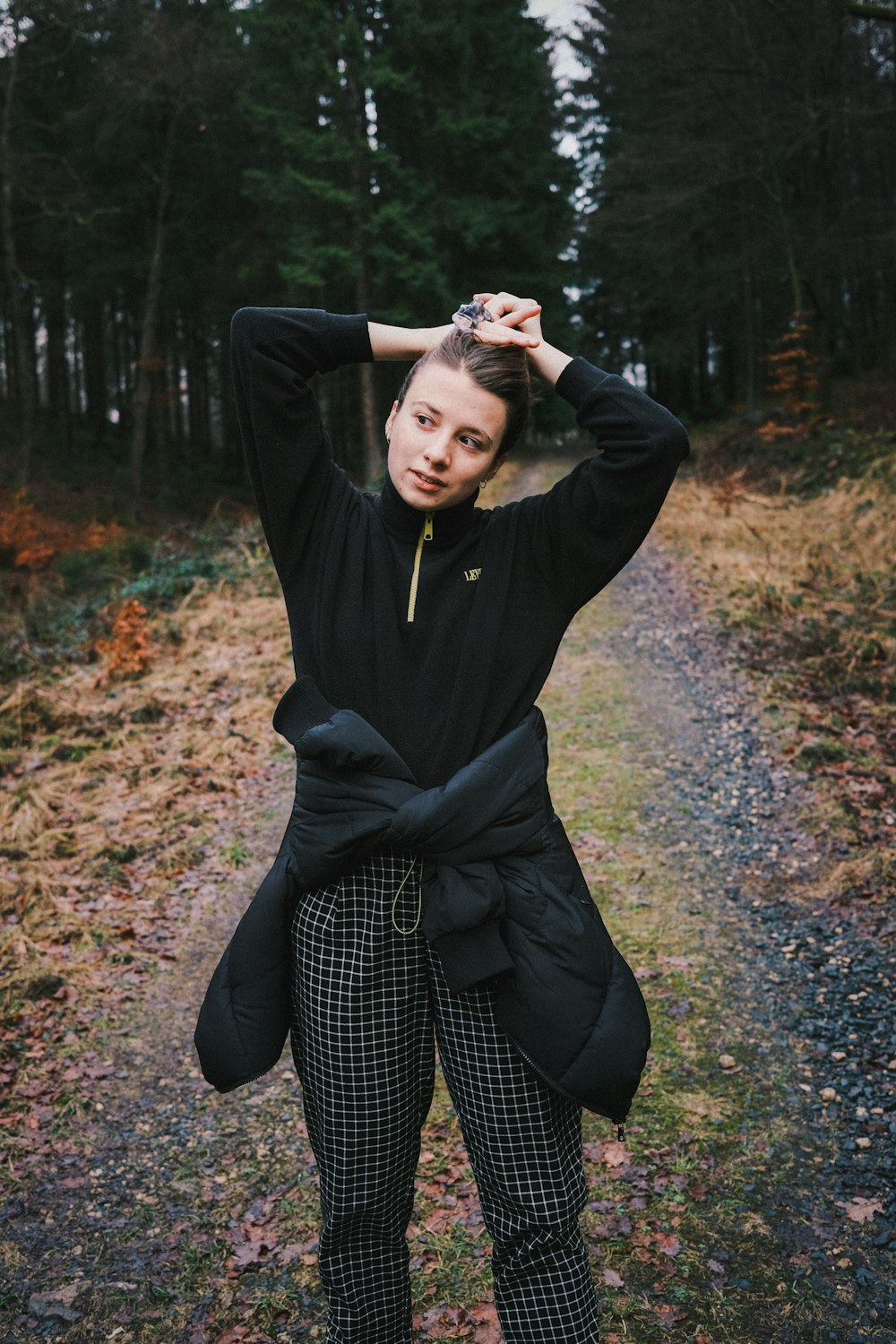 woman in black coat and black and white polka dot pants sitting on ground with dried