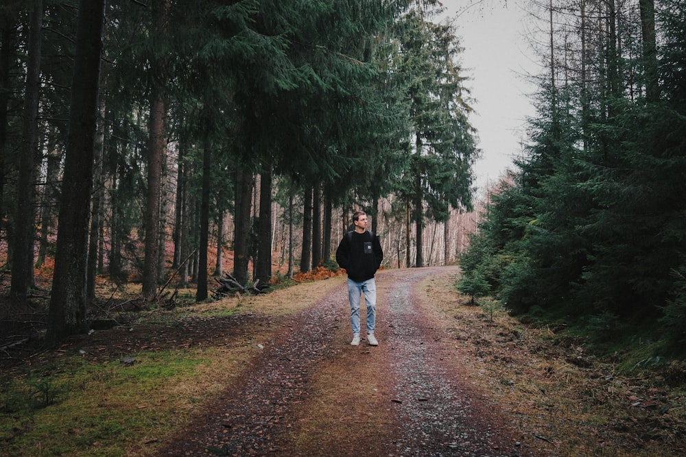 woman in black jacket walking on pathway between trees during daytime