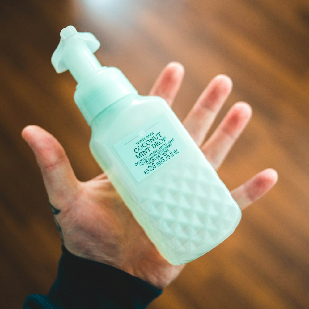Persona sosteniendo una botella de plástico blanco con bomba