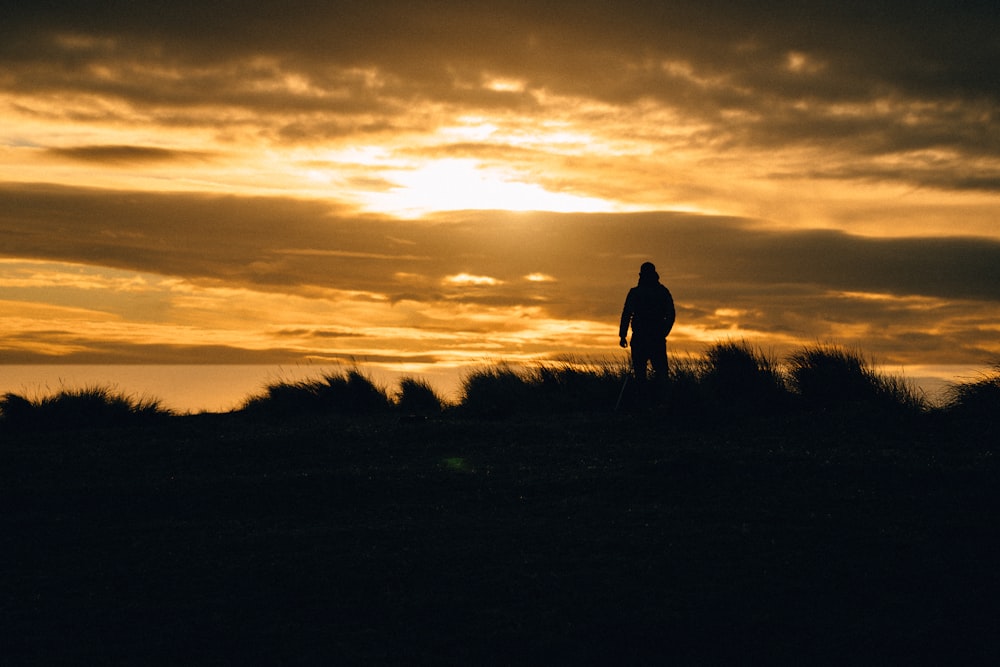 silhueta do homem em pé no campo de grama durante o pôr do sol