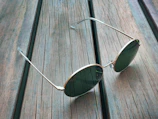 Sunlit outdoor shot of round vintage-style sunglasses with gold frames.