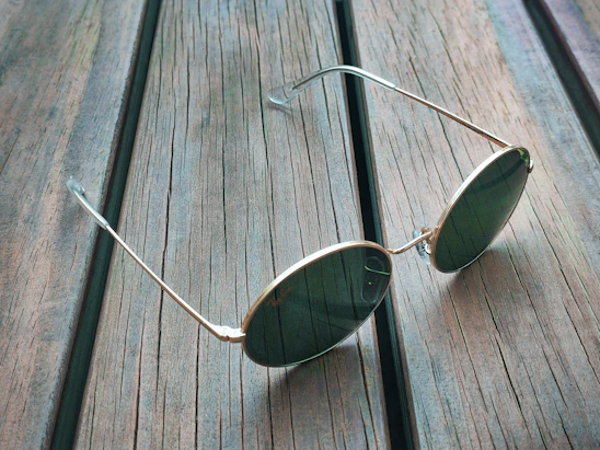 Close-up of a pair of handcrafted wood frame sunglasses resting on a rustic wooden table with sunlight casting warm shadows.