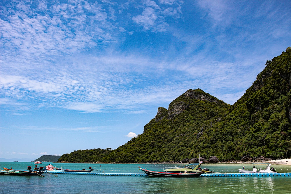 white and red boat on sea near green mountain under blue sky during daytime