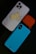 A smartphone with a white case featuring a humorous sticker of a cartoon character in a playful pose is placed alongside an orange AirPods case and a blue phone case with a textured pattern. The arrangement is set against a dark background.