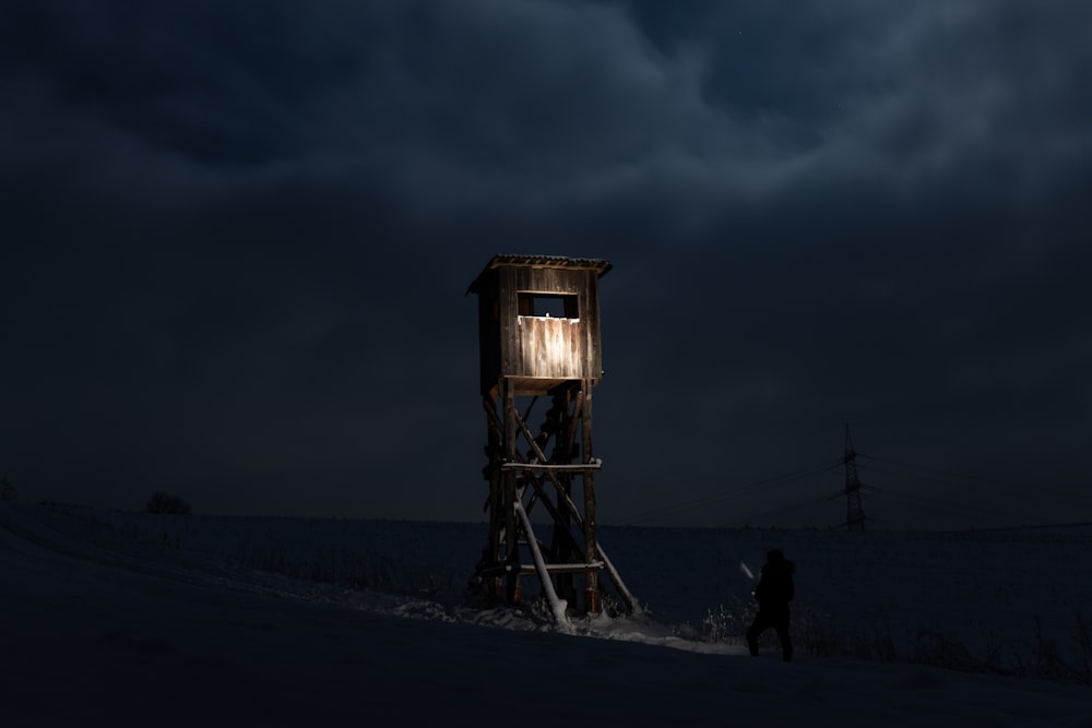 silhueta da pessoa em pé perto da torre de madeira marrom durante a noite