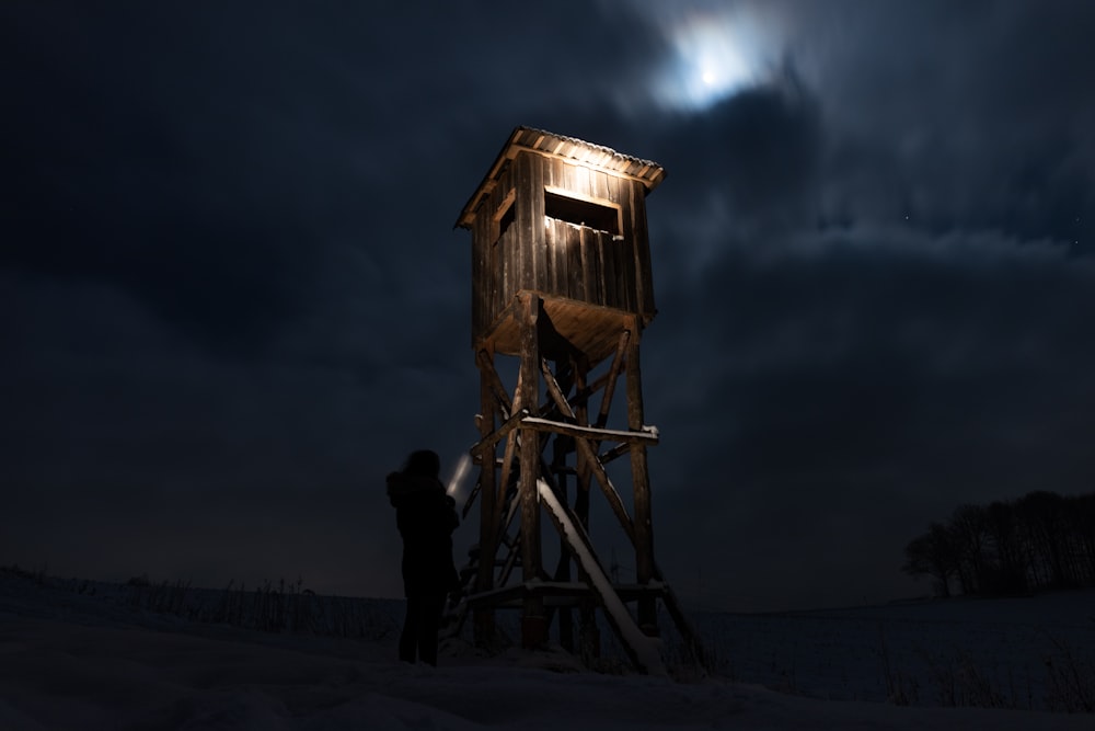 homem em pé perto da casa de madeira marrom durante a noite