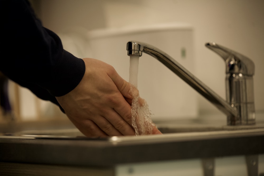 person holding white textile in front of stainless steel faucet
