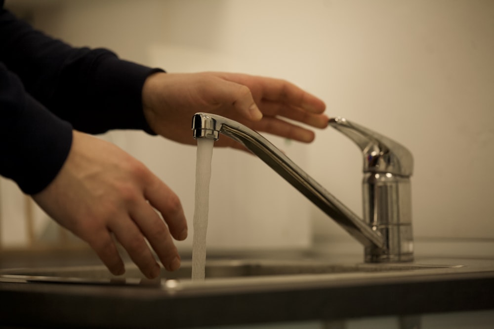 person in black long sleeve shirt holding stainless steel faucet