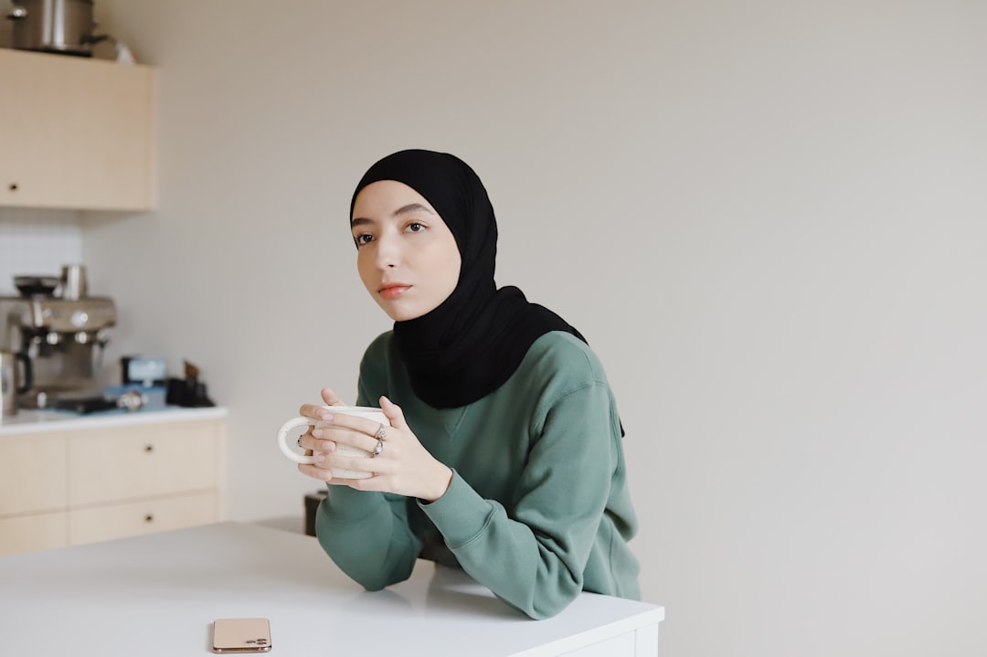 woman in green hijab holding white ceramic mug