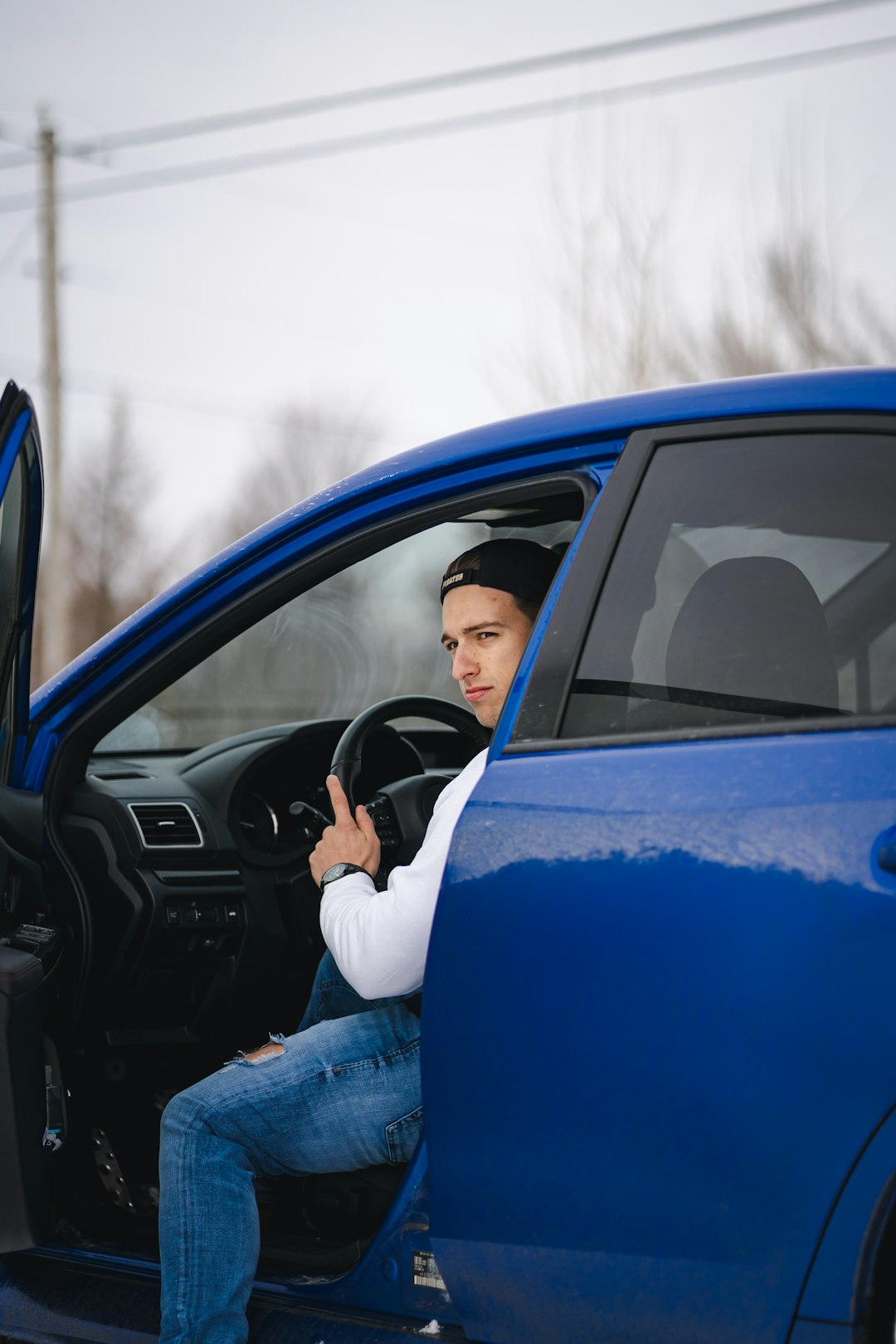 man in black jacket and blue denim jeans leaning on blue car