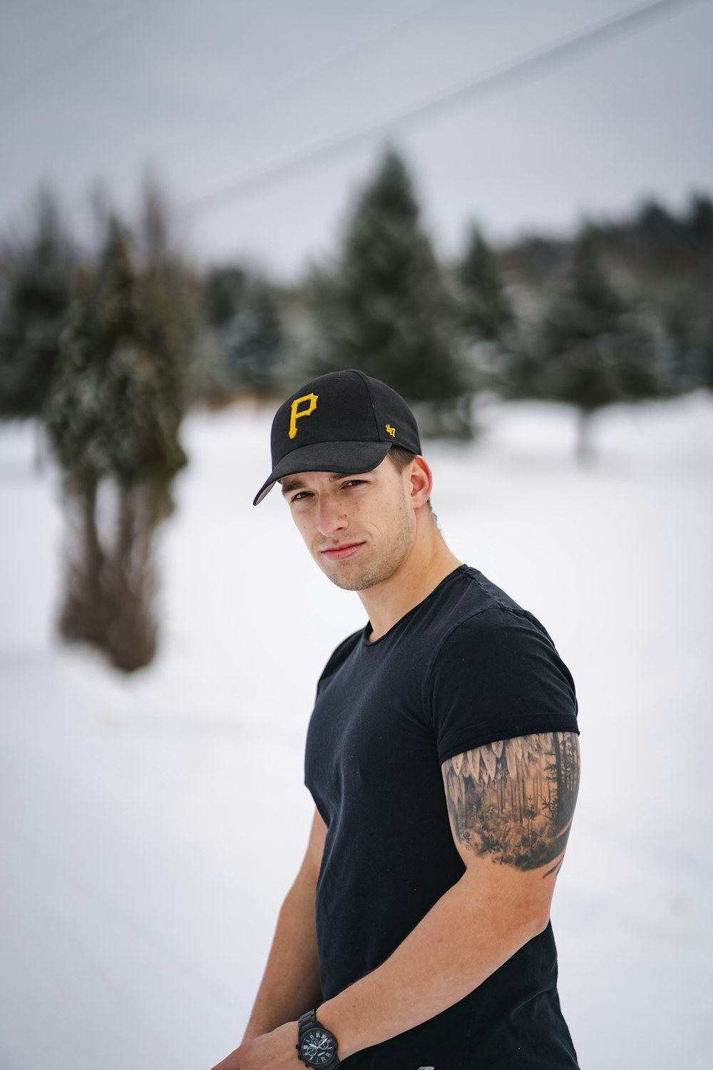 homme en t-shirt à col rond noir et casquette cintrée noire debout sur un sol enneigé