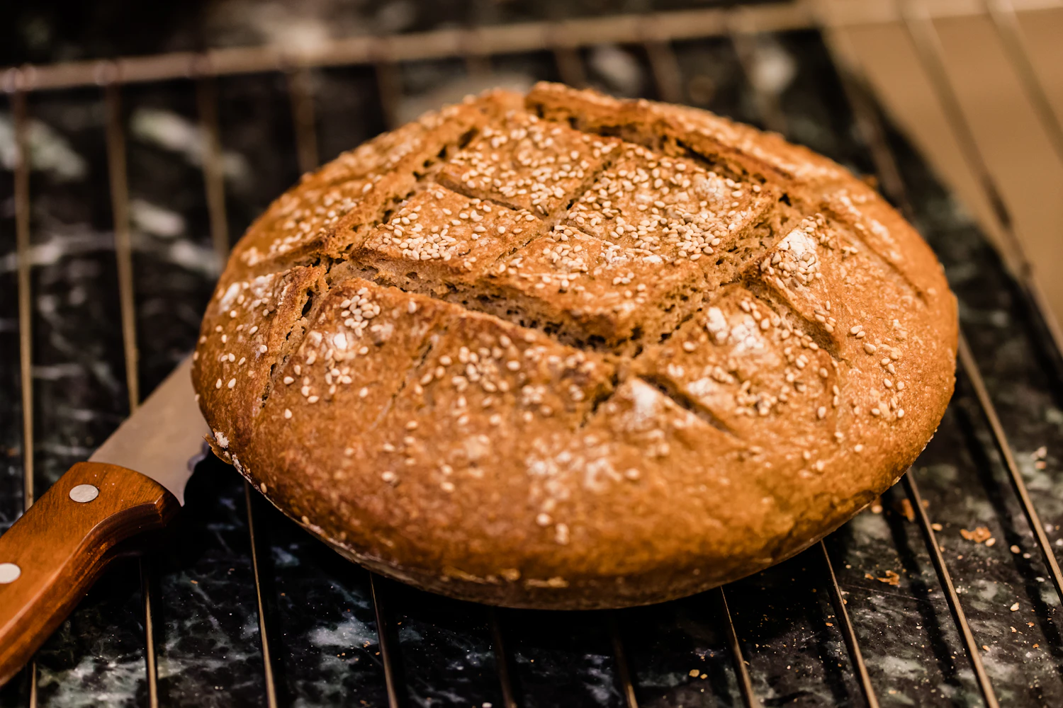 A scored wholegrain boule cooling on a wire rack, crust split along the cut