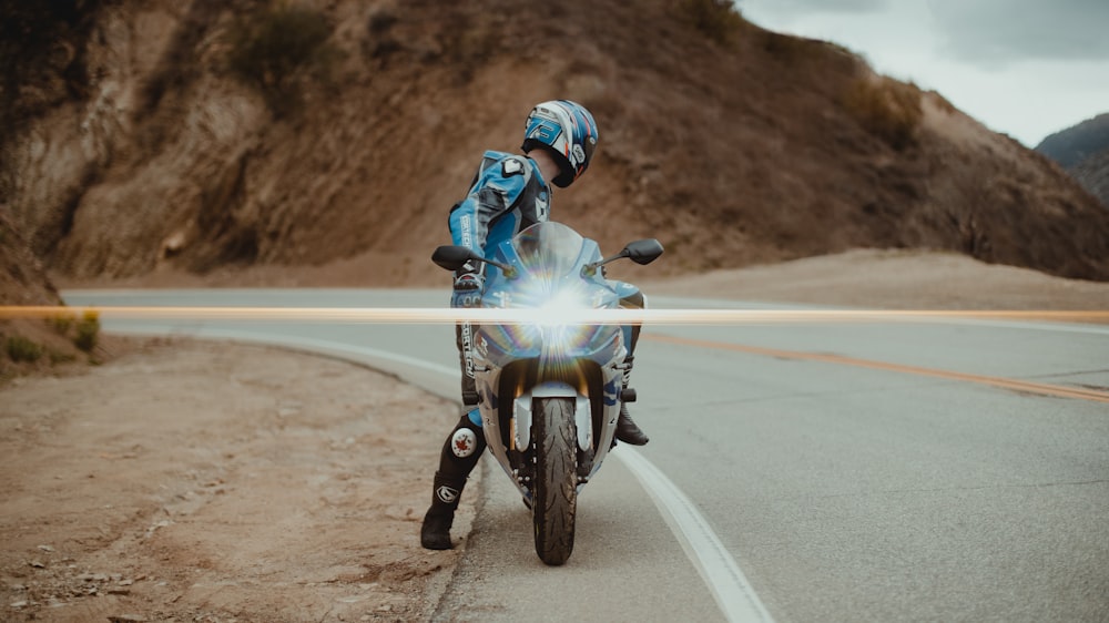 homme en costume de moto bleu et blanc conduisant une moto sur la route pendant la journée