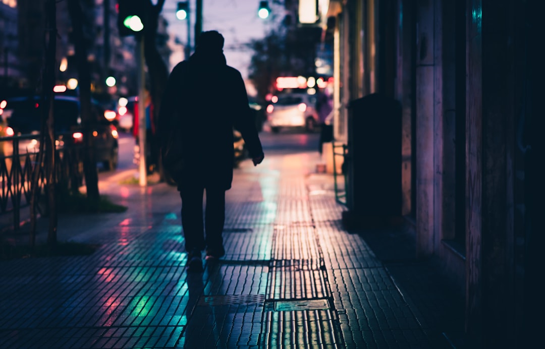 man in black jacket walking on sidewalk during night time