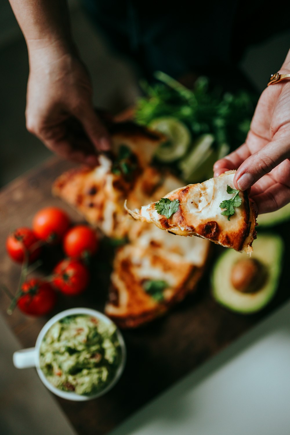 person holding sliced pizza with sliced tomato and green leaves