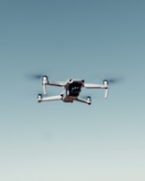 A drone with four rotors is flying against a clear blue sky, capturing an image that emphasizes its mechanical structure and design.