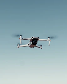 A drone with four rotors is flying against a clear blue sky, capturing an image that emphasizes its mechanical structure and design.