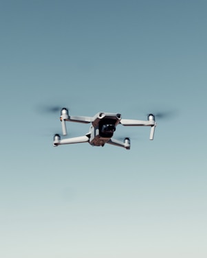 A drone with four rotors is flying against a clear blue sky, capturing an image that emphasizes its mechanical structure and design.