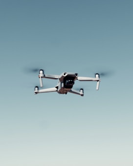 A drone with four rotors is flying against a clear blue sky, capturing an image that emphasizes its mechanical structure and design.