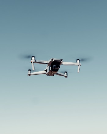 A drone with four rotors is flying against a clear blue sky, capturing an image that emphasizes its mechanical structure and design.