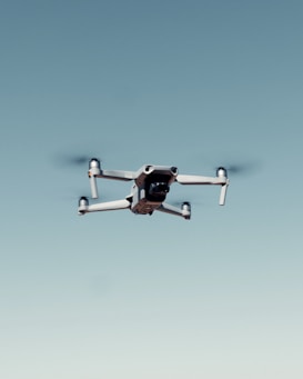 A drone with four rotors is flying against a clear blue sky, capturing an image that emphasizes its mechanical structure and design.
