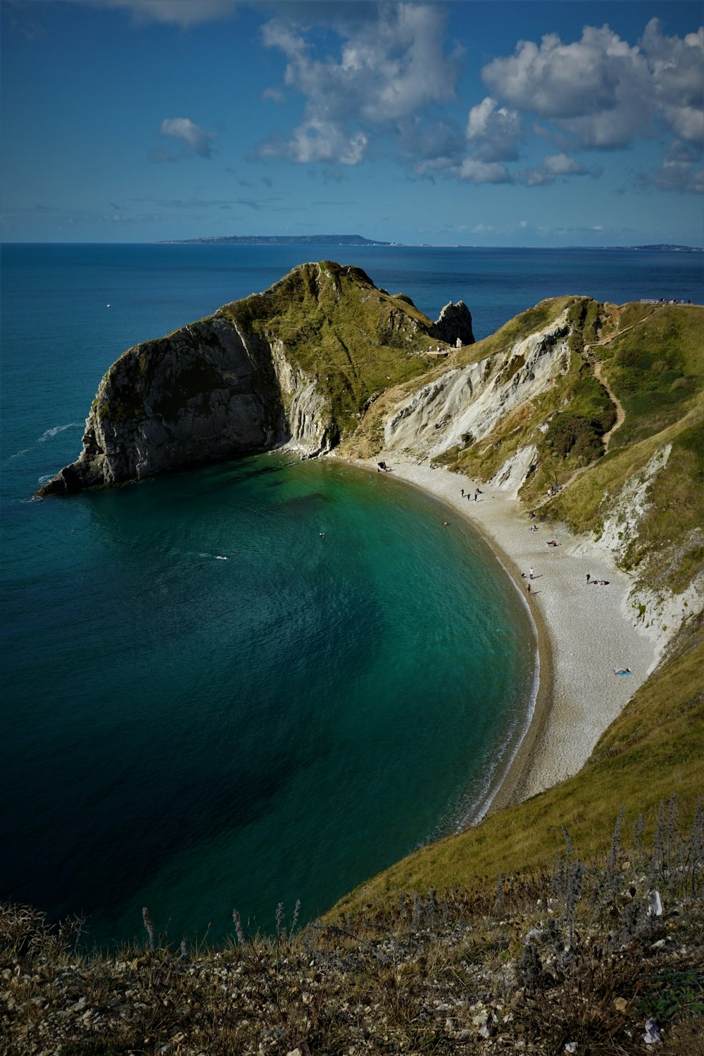 green and brown mountain beside blue sea during daytime