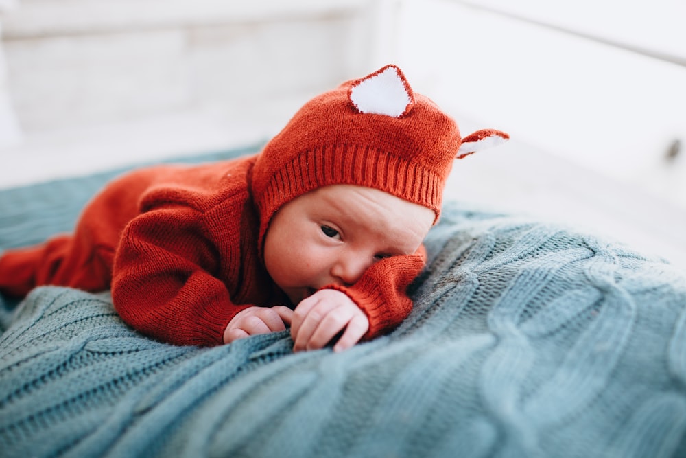 baby in red knit cap lying on blue textile