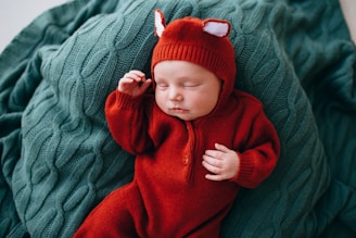 baby in red knit cap and red sweater lying on green textile