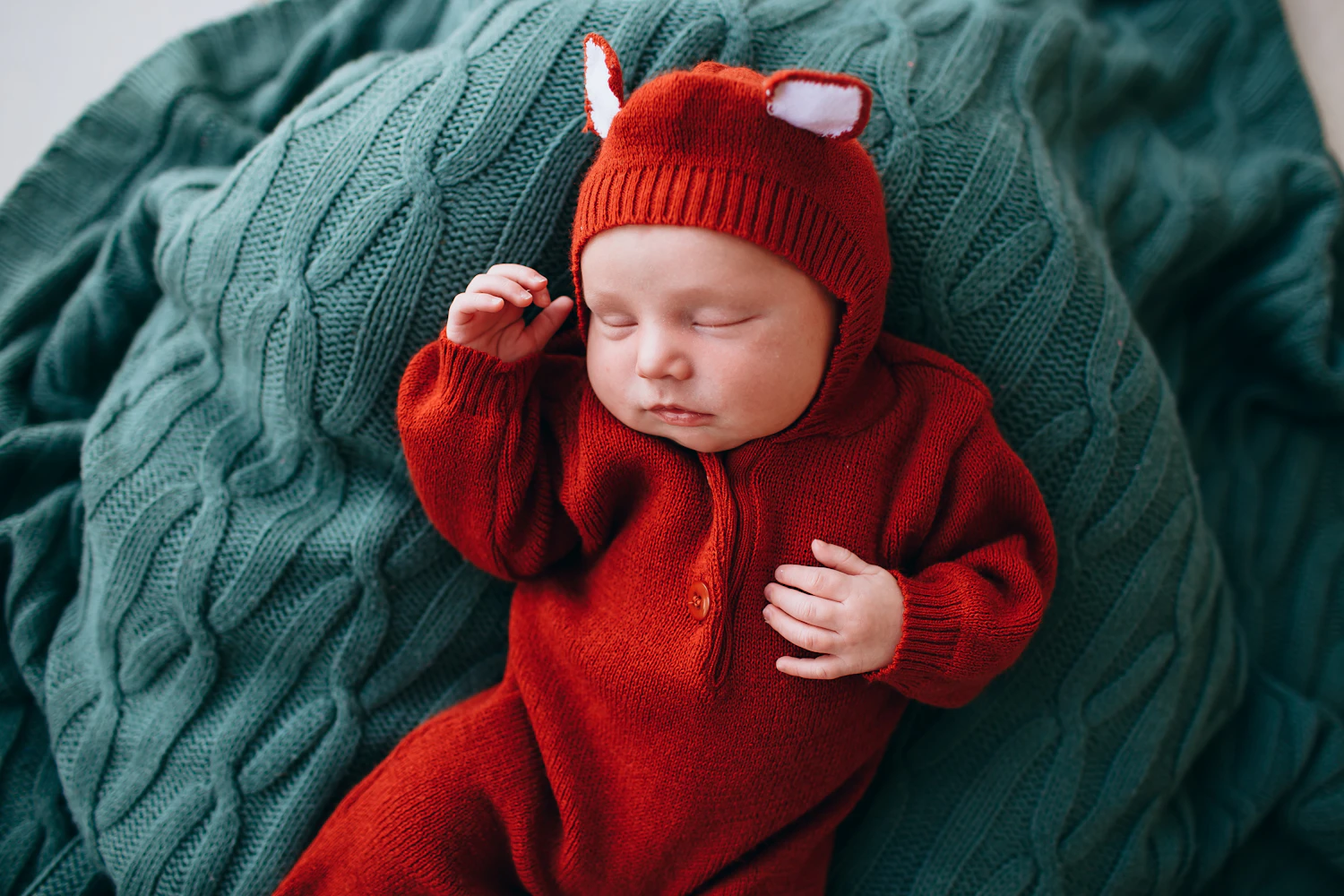 The Søndag first set worn: a knitted suit and hat on a cable blanket