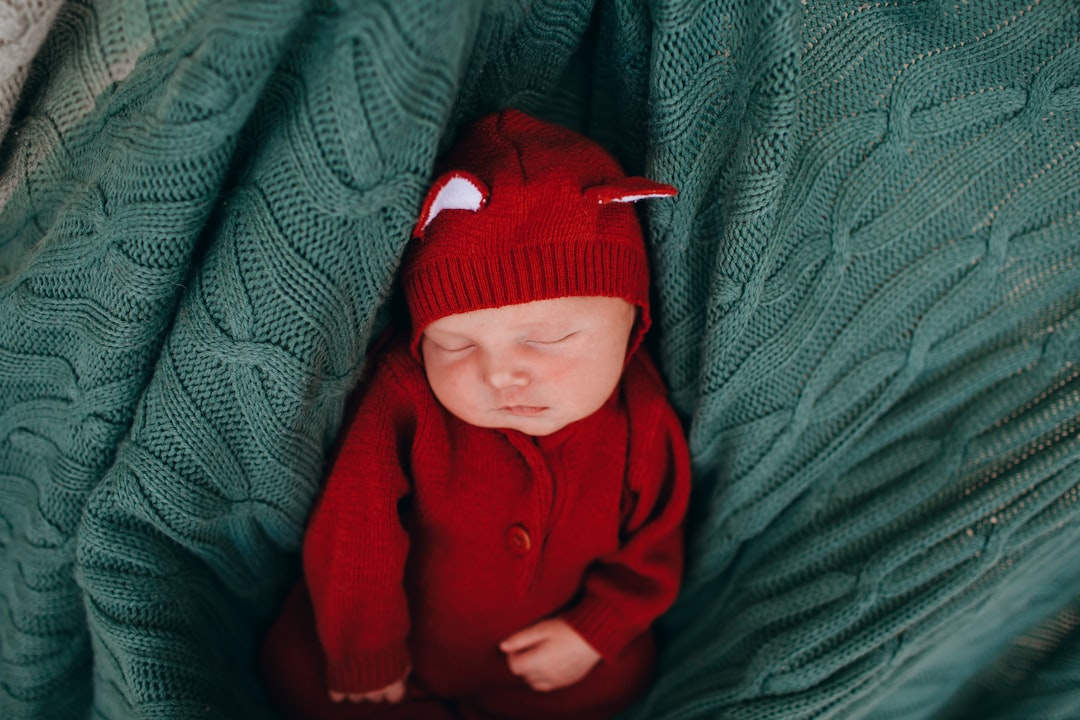 baby in red jacket lying on bed