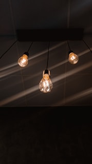 Three hanging lightbulbs emit a warm glow against a dark ceiling, with visible wires extending upward.