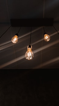 Three hanging lightbulbs emit a warm glow against a dark ceiling, with visible wires extending upward.